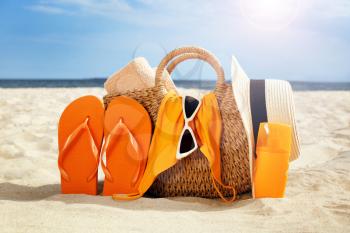 Bag with flip-flops, swimsuit, hat, sunglasses and cosmetics on sand beach�