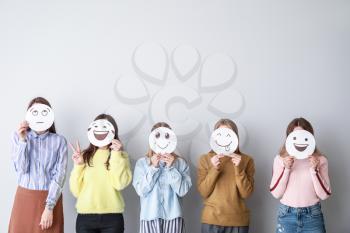 Group of woman covering their faces with drawn emoticons against light background�