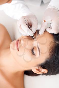 Young woman undergoing eyebrow correction procedure in beauty salon�