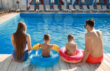 Young family sitting near swimming pool, back view�