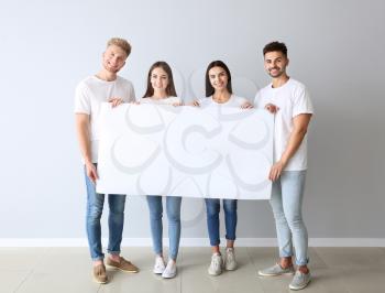 Group of young people in stylish casual clothes and with blank poster near light wall�