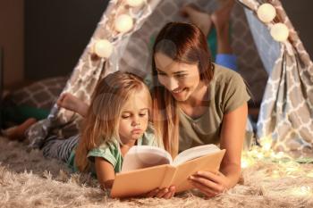 Mother and her little daughter reading book in evening�