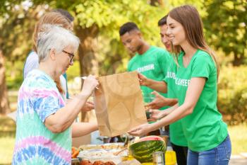 Young volunteers giving food to poor people outdoors�