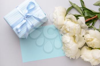 Gift box, blank card and beautiful flowers on light background�
