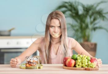 Angry woman with taped mouth, healthy and unhealthy food in kitchen. Diet concept�