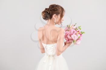 Beautiful young bride with wedding bouquet on light background, back view�