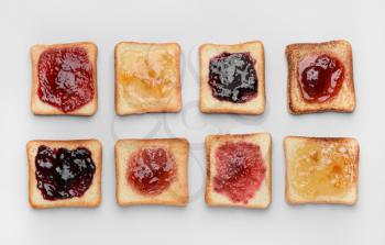 Tasty toasted bread with different jams on white background�