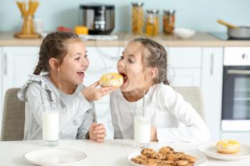 Portrait of cute twin girls eating donuts with milk in kitchen�
