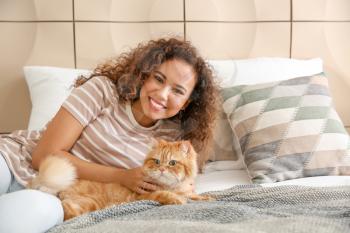 Young African-American woman with cute cat at home�