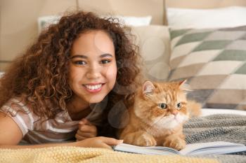 Young African-American woman with cute cat reading book at home�