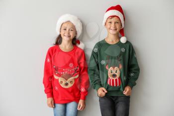 Funny children in Christmas sweaters and Santa hats on light background�
