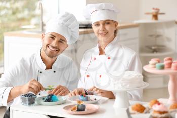 Young confectioners decorating tasty dessert in kitchen�