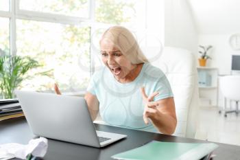 Angry mature woman with laptop working in office�
