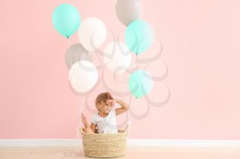 Little girl sitting in basket with balloons near color wall�