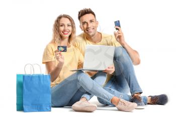 Young couple with credit cards, shopping bags and laptop on white background�