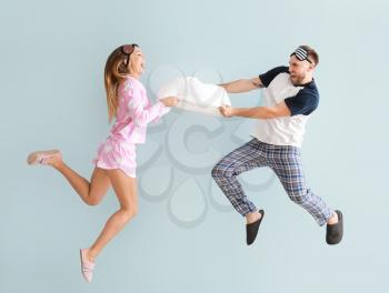 Young couple fighting for pillow on color background�