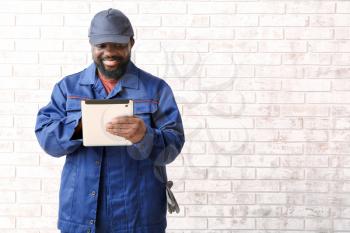 African-American car mechanic with tablet computer near brick wall�