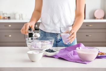 Woman putting tasty blueberry ice cream into glass in kitchen�