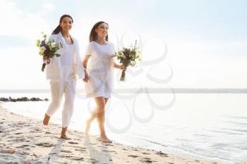 Beautiful lesbian couple walking along a river bank on their wedding day�