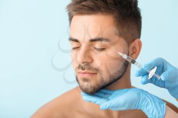 Handsome man receiving filler injection on color background�