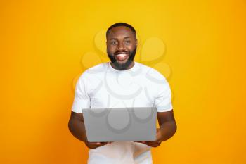 Handsome African-American man with laptop on color background�