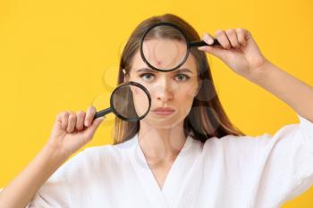 Portrait of young woman with acne problem and magnifying glasses on color background�