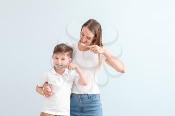 Portrait of mother and her little son brushing teeth on light background�