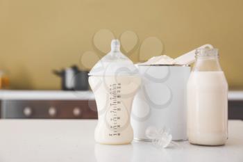 Bottles of milk and jar with baby formula on table in kitchen�