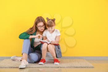 Cute little girl and her mother reading books near color wall�