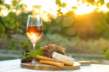 Glass of wine with snacks on wooden table in vineyard�