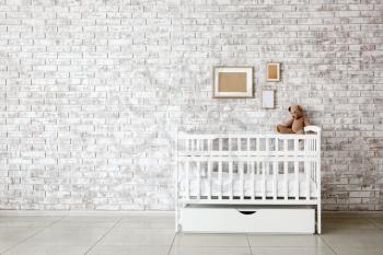 Stylish baby bed near brick wall in interior of children's room�