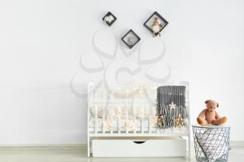 Stylish baby bed near white wall in interior of children's room�