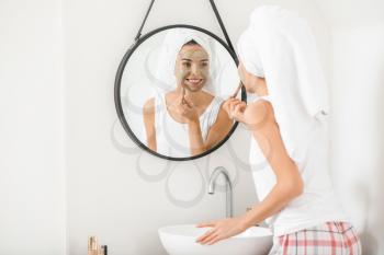 Beautiful young woman applying facial mask at home�