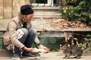 Poor man sharing food with homeless cat outdoors�