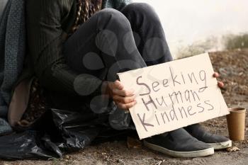 Poor homeless man holding cardboard with text SEEKING HUMAN KINDNESS outdoors�
