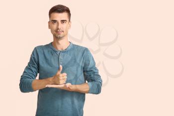 Young deaf mute man using sign language on color background�