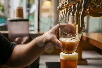 Barman pouring fresh beer in glass, closeup�