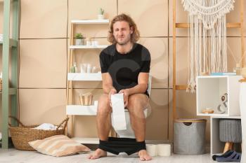 Young man suffering from constipation while sitting on toilet bowl at home�