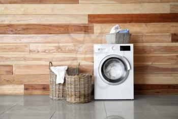 Modern washing machine with laundry near wooden wall�