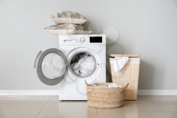 Modern washing machine with laundry near white wall�
