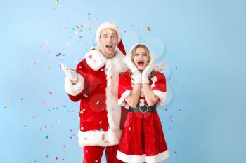 Happy couple dressed as Santa Claus with flying confetti on color background�