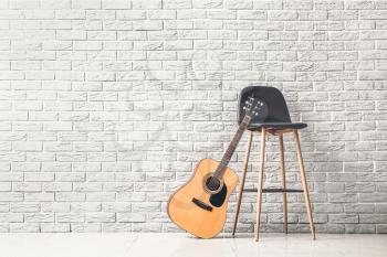 Modern acoustic guitar and chair near white brick wall�