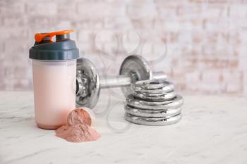 Bottle of protein shake with dumbbell on light background�