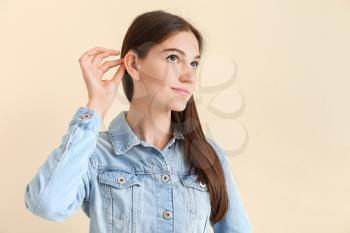 Young woman with hearing aid on color background�