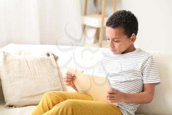 Little African-American boy with hearing aid reading book at home�