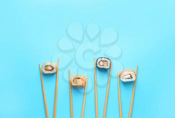Tasty sushi rolls and chopsticks on color background�