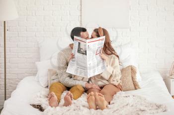 Beautiful young couple reading newspaper on bed at home�