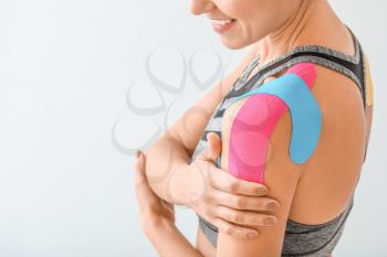 Sporty woman with physio tape applied on shoulder against light background, closeup�
