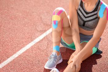 Sporty woman with physio tape applied on knee at stadium�