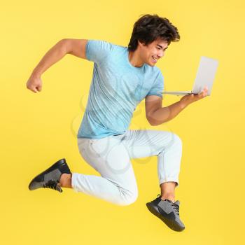 Jumping male Asian programmer with laptop on color background�